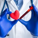 Diagnósticos médicos de laboratório, testes de coração e foto do conceito cardiovascular. Médico ou técnico de laboratório segura em uma mão um tubo de ensaio de laboratório com sangue, na outra mão - figura de coração